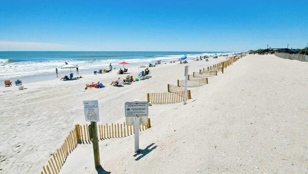 Ein sandiger Strand mit einer Holzlattenzaun, Strandkörben und entspannten Personen.