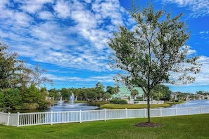 A park with a fountain, a white fence, and a building with a green roof. - Ocean Keyes 3722 The Gleaming Starfish (North Myrtle Beach)