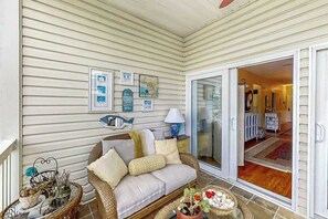 A covered porch with a wicker sofa, a table with decorative items, and a sliding glass door leading to an interior space. - Ocean Keyes 3722 The Gleaming Starfish (North Myrtle Beach)