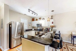 A modern kitchen with stainless steel appliances, a central island with seating, and a decorative vase. - Ocean Keyes 3722 The Gleaming Starfish (North Myrtle Beach)
