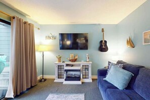 A living room with a blue sofa, a fireplace, a mounted TV, and a guitar. - The Golden Sailboat B-139 (Myrtle Beach)