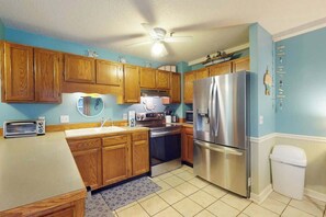 A kitchen with wooden cabinets, a stainless steel refrigerator, a microwave, and a toaster. - The Golden Sailboat B-139 (Myrtle Beach)