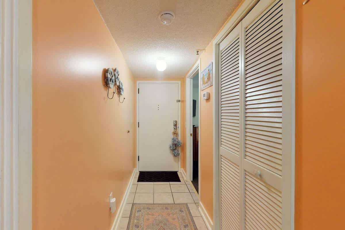A hallway with a door, a wall-mounted clock, and a patterned rug.