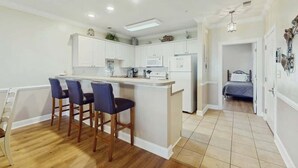 A modern kitchen with a central island, bar stools, and a dining area. - Turtle Cove Unit #204 (Myrtle Beach)
