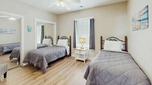 A bedroom with two beds, a ceiling fan, a bedside table with a lamp, and a window with curtains. - Turtle Cove Unit #204 (Myrtle Beach)