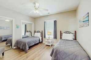 Ein Schlafzimmer mit zwei Betten, einem Deckenventilator, einem Nachttisch mit Lampe und einem Fenster mit Vorhängen.