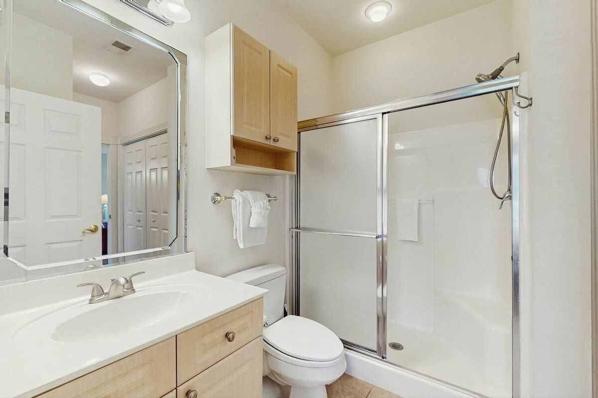 Une salle de bain avec un lavabo blanc, des toilettes, un espace douche et un miroir.