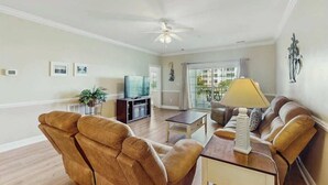 A living room with a sofa, a coffee table, a television, and a ceiling fan. - Turtle Cove Unit #204 (Myrtle Beach)