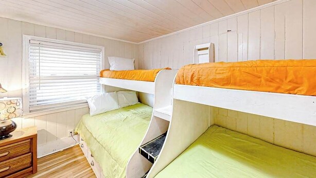A bunk bed room with two beds, a window with blinds, a bedside table, and a wall-mounted light fixture. - Seahorse Serenity Retreat (North Myrtle Beach)