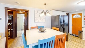 A dining area with a white table, blue chairs, a chandelier, and a refrigerator. - Seahorse Serenity Retreat (North Myrtle Beach)