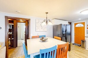 A dining area with a white table, blue chairs, a chandelier, and a refrigerator. - Seahorse Serenity Retreat (North Myrtle Beach)