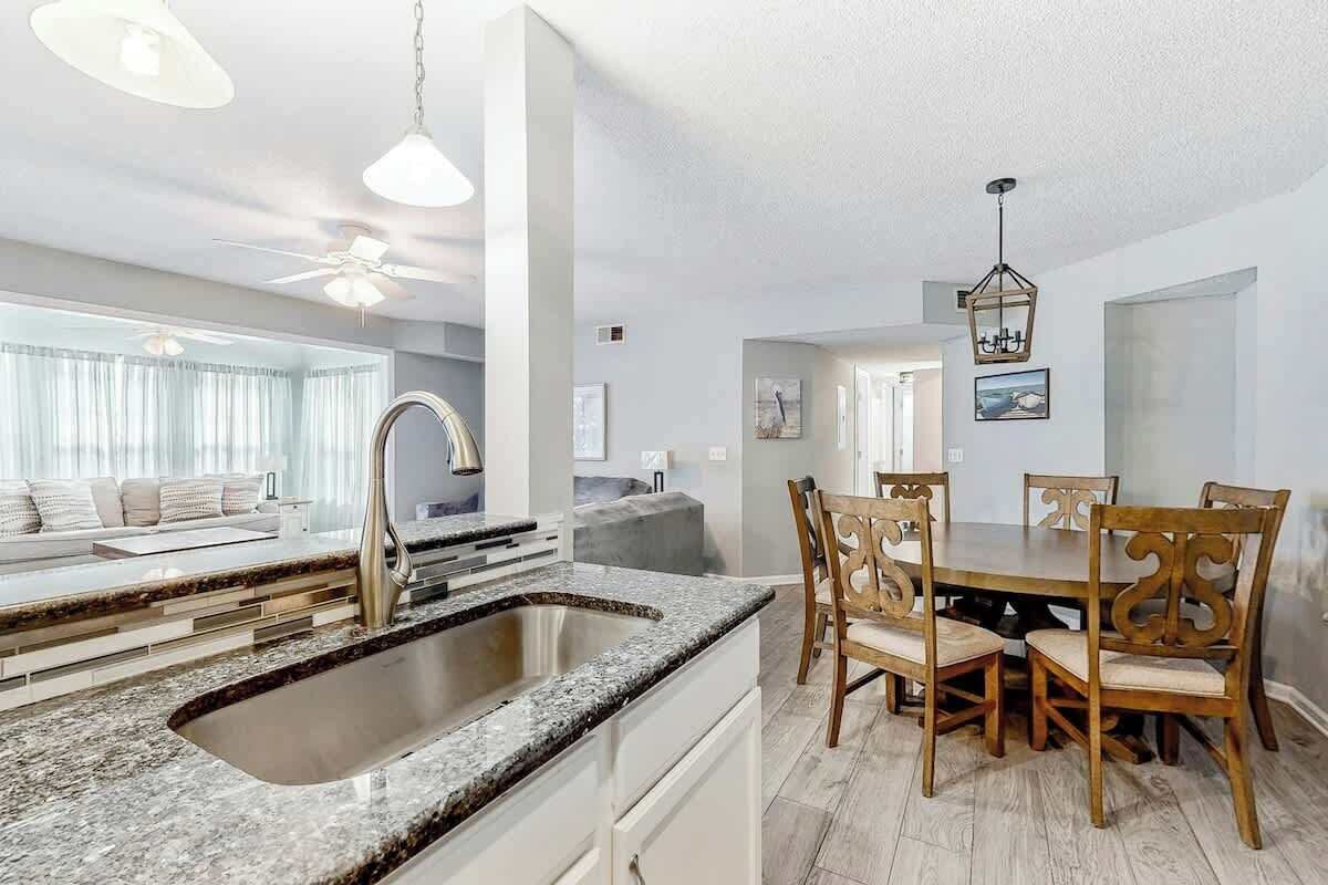 A modern kitchen with a granite countertop, a sink, and a dining area with wooden chairs and a table.