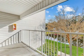 Un balcon donnant sur un étang et des arbres, avec une balustrade blanche et une pancarte sur le mur.