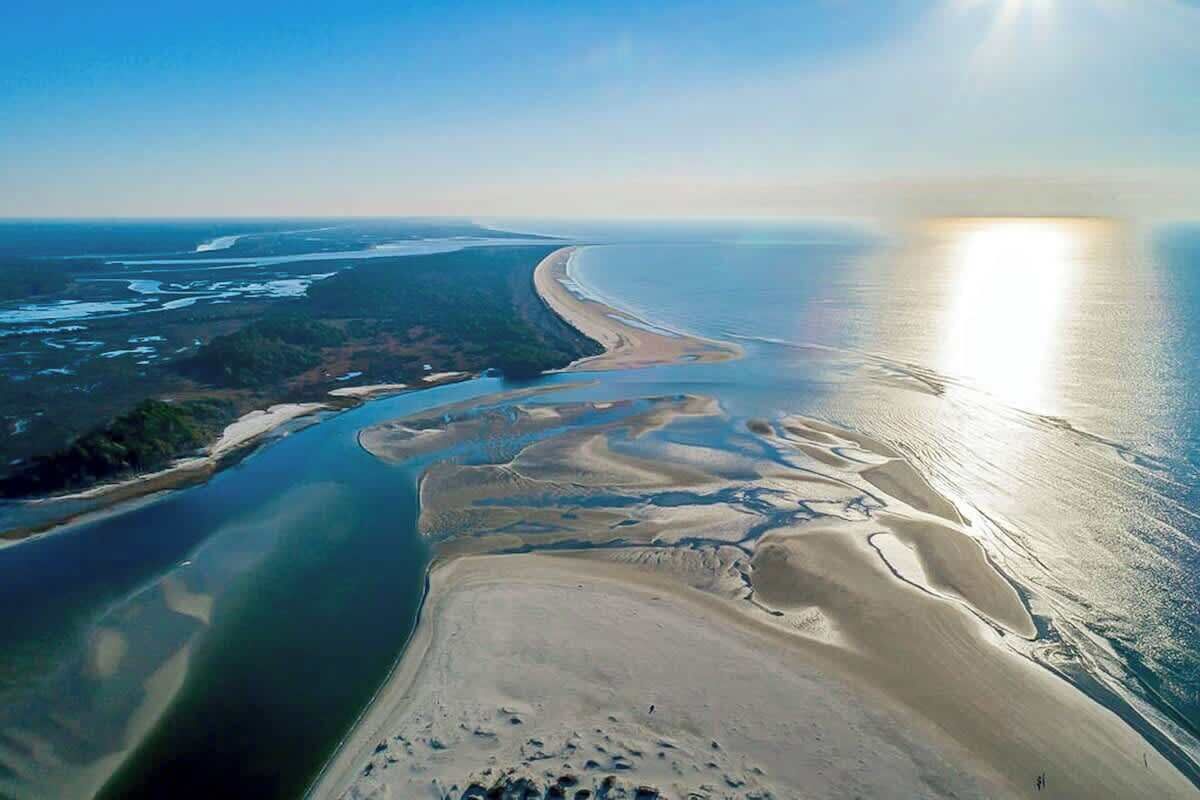 An aerial view of a coastal landscape with a beach, sand dunes, and a river or bay.