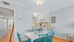 A modern kitchen with white cabinets, a microwave, and a dining area with a white table and teal chairs. - Inlet Point Villas 10-D (North Myrtle Beach)