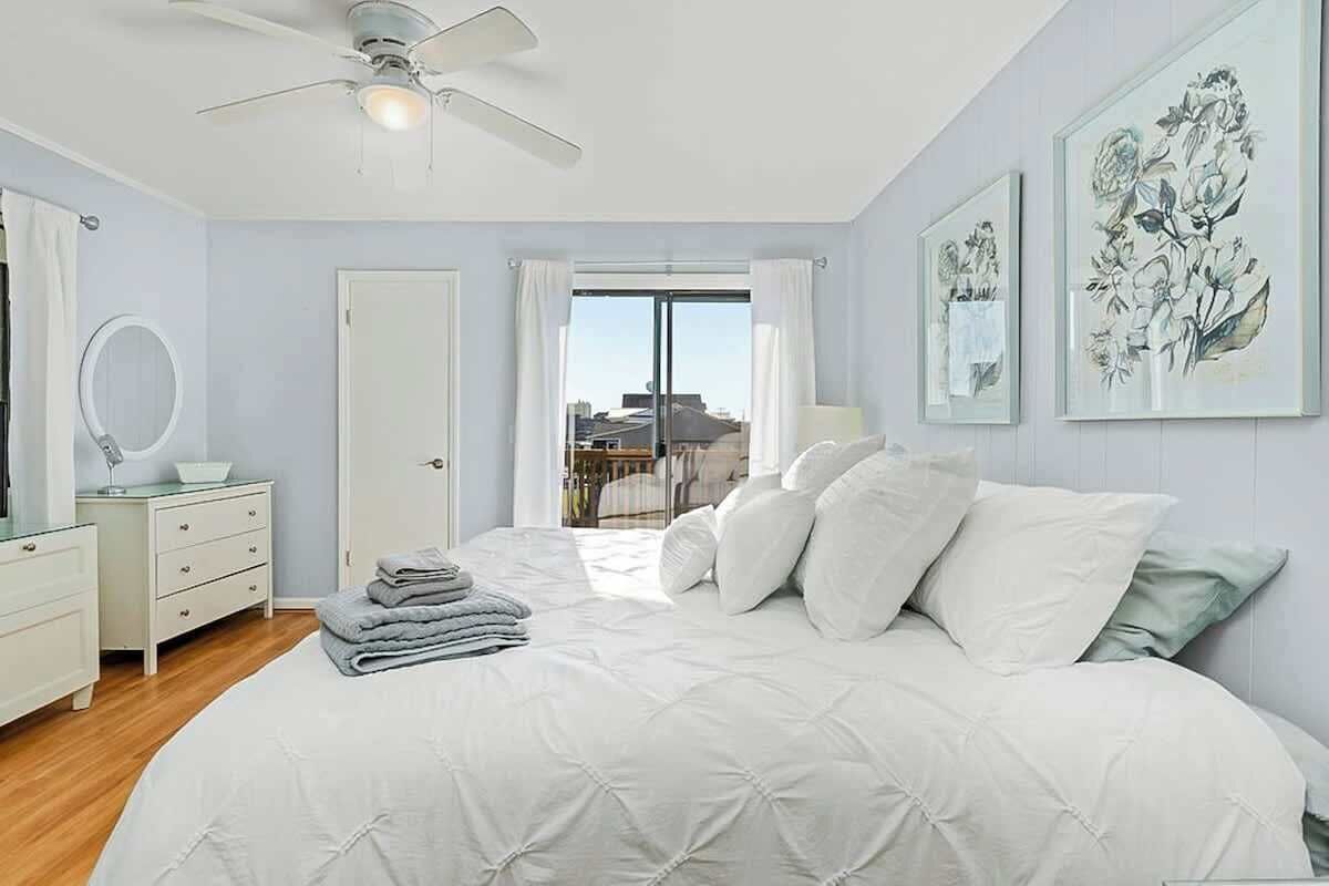 A bedroom with a bed, a ceiling fan, a door, a window, and artwork on the wall.