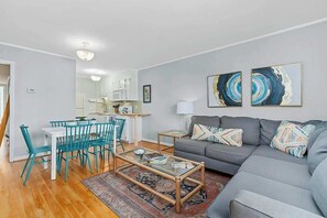 A modern living room with a grey sofa, teal chairs, a glass coffee table, and abstract wall art. - Inlet Point Villas 10-D (North Myrtle Beach)
