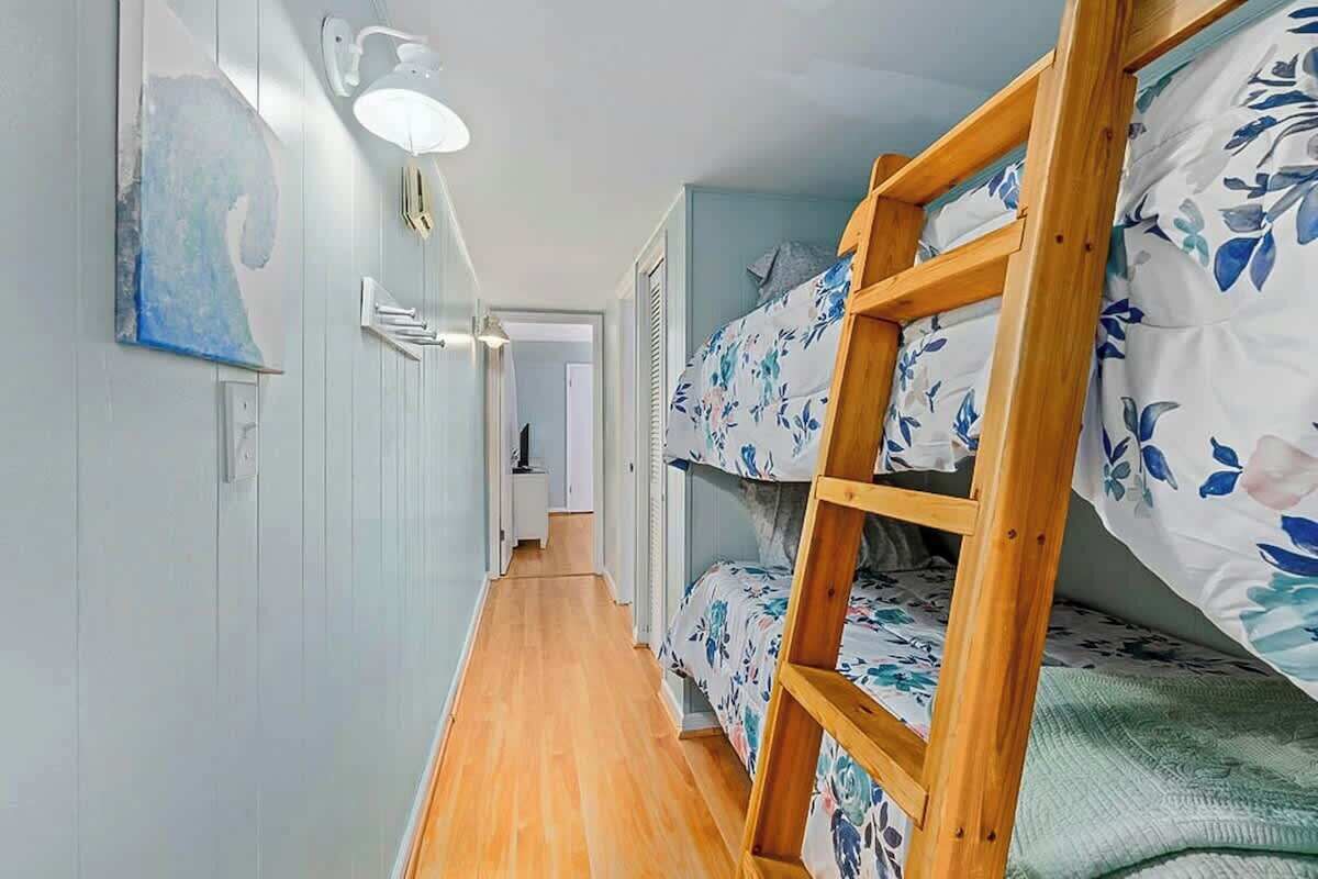 Um corredor estreito com beliches de um lado e uma porta no final.