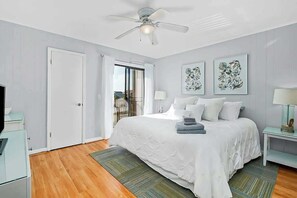A bedroom with a bed, two bedside lamps, a ceiling fan, and a view through a glass door. - Inlet Point Villas 10-D (North Myrtle Beach)