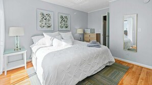 A bedroom with a bed, a nightstand, a lamp, a dresser, a mirror, and a door leading to another room. - Inlet Point Villas 10-D (North Myrtle Beach)