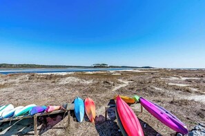 Eine Reihe bunter Kajaks auf einem Holgestell am Strand bei klarem Himmel.