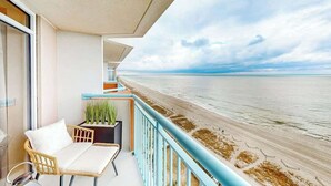 En balkon med udsigt over stranden, en stol, et lille bord og en potteplante.