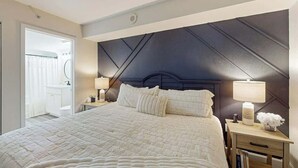 Et hotelværelse med en stor seng, et natbord med en lampe og udsigt til badeværelset.