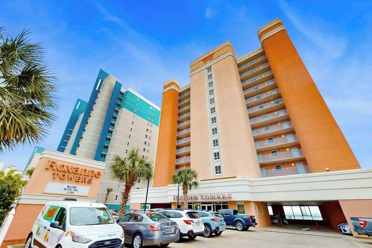 A hotel with multiple high-rise buildings, a parking area, and a sign welcoming guests.