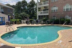 Ein Pool mit einer Ziegelterrasse, Liegestühlen und einem Gebäude mit Balkon im Hintergrund.
