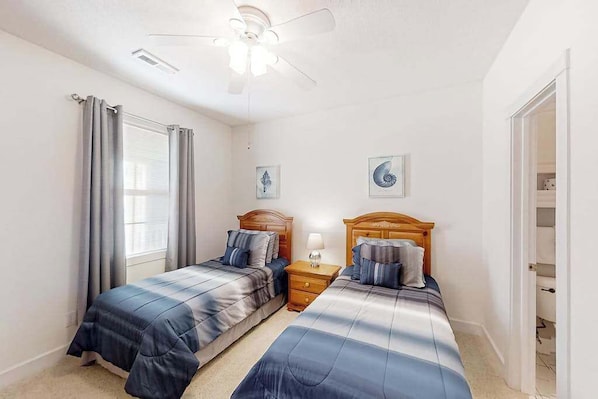 A bedroom with two beds, a ceiling fan, and a window with curtains. - Gardens at Cypress Bay 14-204 (Little River)