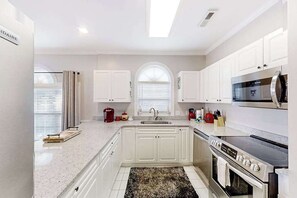A modern kitchen with white cabinetry, a stainless steel oven, and a microwave. - Gardens at Cypress Bay 14-204 (Little River)