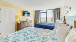 Ein Hotelzimmer mit zwei Betten, einem Fernseher, einer Kommode und einem Fenster mit Vorhängen.