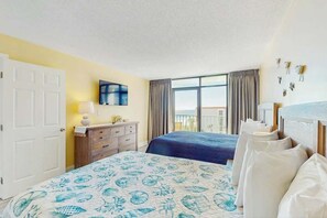 Ein Hotelzimmer mit zwei Betten, einem Fernseher, einer Kommode und einem Fenster mit Vorhängen.