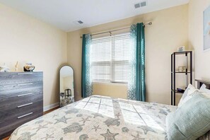 A bedroom with a bed, dresser, mirror, window with curtains, and a nightstand. - Sun and Sand Retreat (Myrtle Beach)