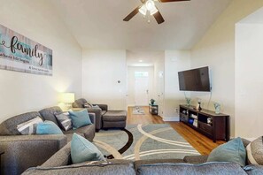 A living room with a sofa set, a television, a ceiling fan, and a wall with a family-themed sign. - Sun and Sand Retreat (Myrtle Beach)