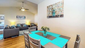 Een eetgedeelte met een tafel voor vier personen, een plafondventilator en een schilderij aan de muur.