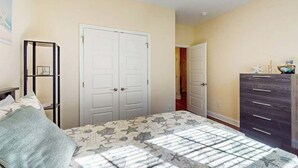 Een slaapkamer met een bed, twee witte deuren, een dressoir en een plankunit.