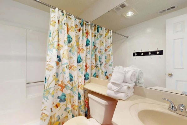 Um banheiro com cortina de chuveiro estampada com flores, pia com espelho e porta-toalhas com toalhas.