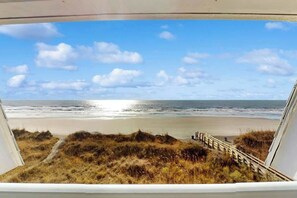 Blick auf einen Strand durch ein Fenster, mit einer hölzernen Promenade, die zum Ufer führt.