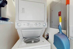A front-loading washing machine with a control panel, a blue cleaning brush, and a water heater with a red emergency stop button. - Ocean Wave Retreat Home (North Myrtle Beach)