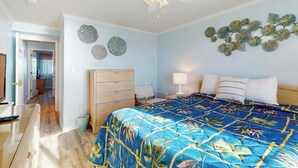 Quarto com cama, ventilador de teto, cômoda e decoração nas paredes.