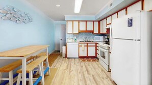 Uma cozinha compacta com área de refeições, armários brancos, micro-ondas e geladeira.