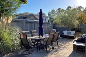 Eine Terrasse im Freien mit Esstisch und Stühlen, einer Sitzecke und einem Sonnenschirm.