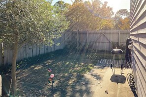 A backyard with a tree, a barbecue grill, and a fence. - Tide the Knot At Last (North Myrtle Beach)