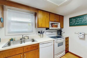 A kitchen with wooden cabinets, a white countertop, a built-in oven, and a wall-mounted sign. - Tide the Knot At Last (North Myrtle Beach)