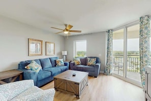 A living room with a sofa set, a coffee table, and a ceiling fan. - Tilghman Condos #1018 (North Myrtle Beach)