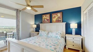 Un dormitorio con una cama, dos lámparas de noche, un ventilador de techo y una obra de arte en la pared.