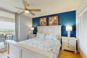 A bedroom with a bed, two bedside lamps, a ceiling fan, and artwork on the wall. - Tilghman Condos #1018 (North Myrtle Beach)