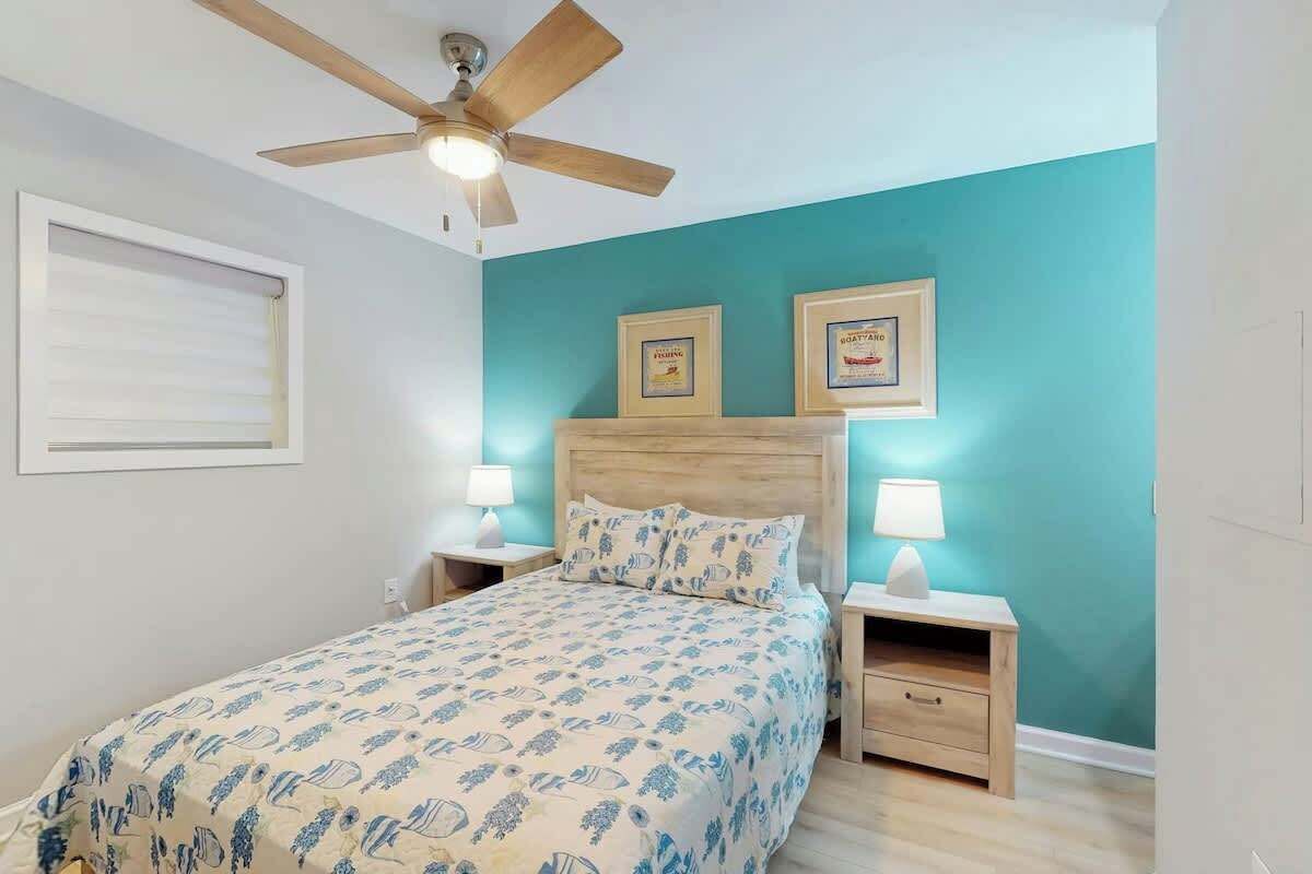 Un dormitorio con una cama, dos mesitas de noche, un ventilador de techo y dos certificados enmarcados en la pared.