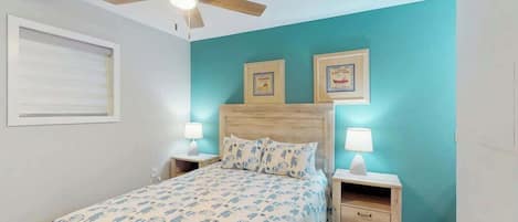 Un dormitorio con una cama, dos mesitas de noche, un ventilador de techo y dos certificados enmarcados en la pared.